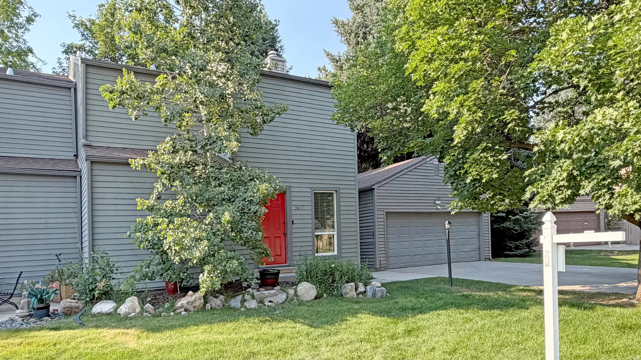 Gray siding exterior featuring a red entry door, and mature landscaping
