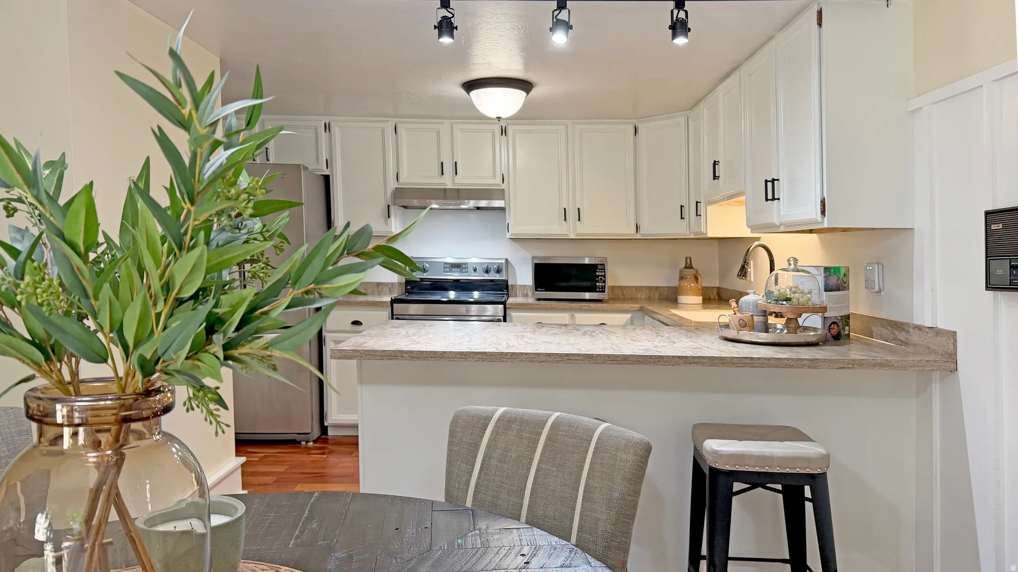 Kitchen featuring white cabinetry, stainless steel appliances, track lighting, a peninsula with seating, and wood-finish flooring