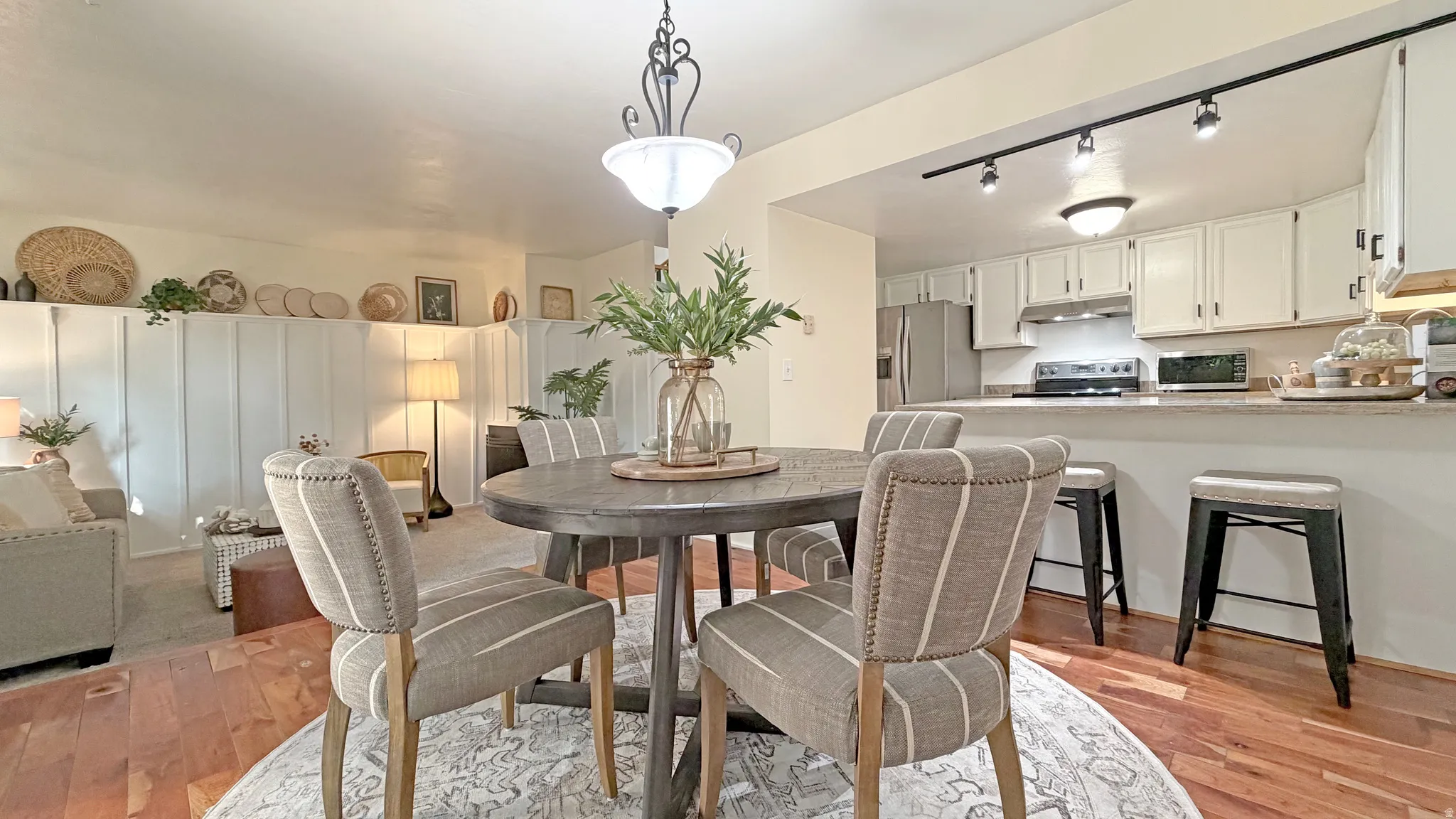 Open-concept dining area with wood-finish flooring, featuring a built-in kitchen pass-through and track lighting