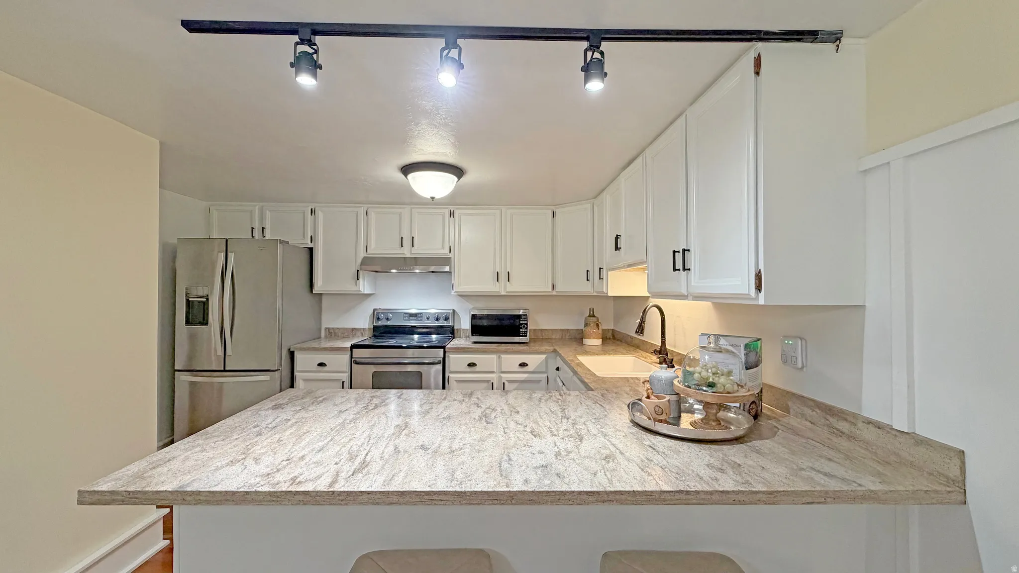 Kitchen featuring a spacious peninsula with a granite countertop, white cabinetry with dark hardware, stainless steel appliances, and track lighting