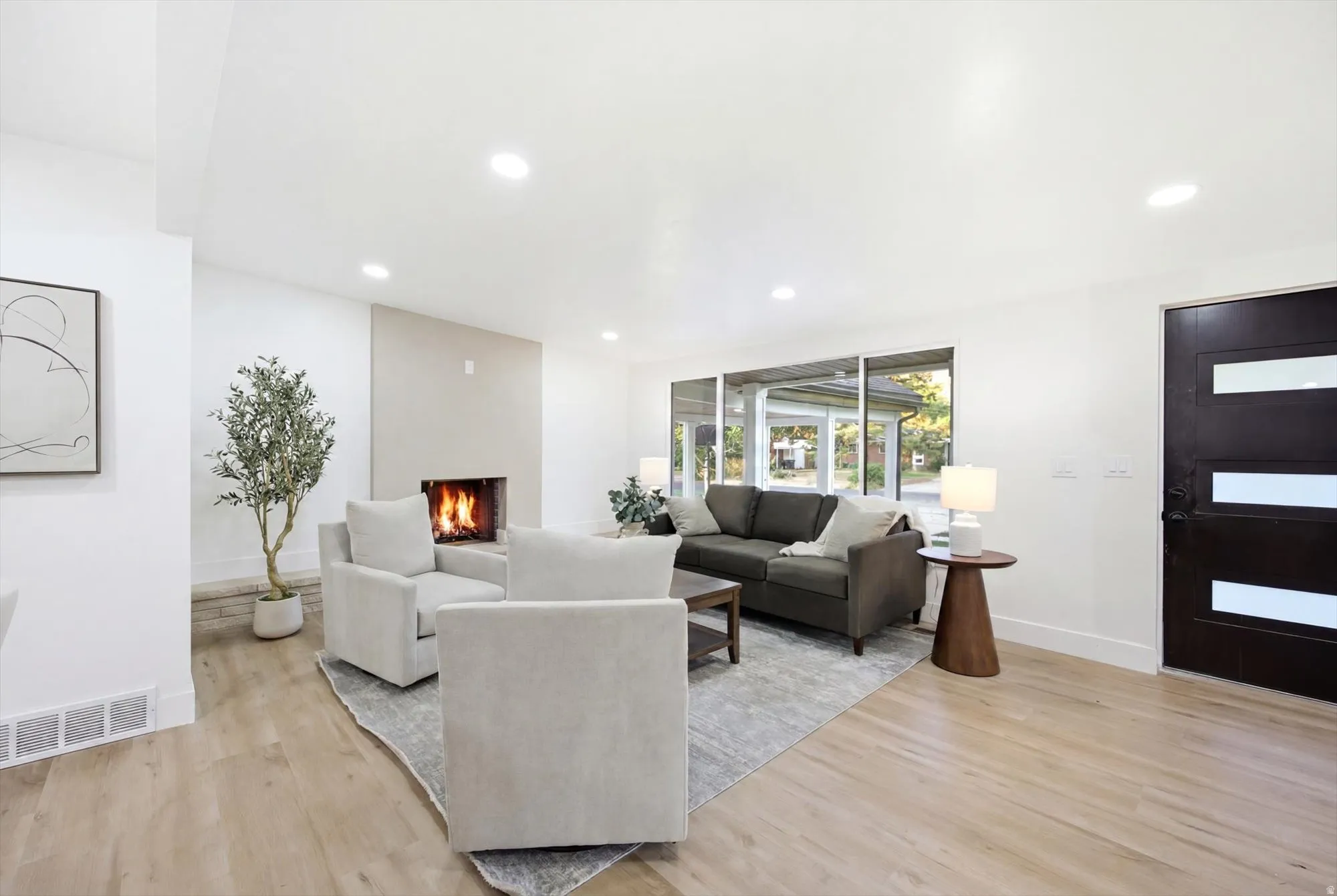 Spacious living area featuring wood-finish flooring, a modern fireplace with a light-toned surround, large picture windows, and recessed lighting