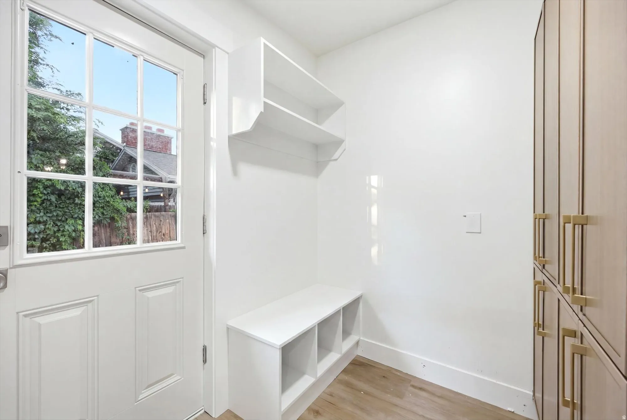 Entryway featuring a paneled door with windowpanes, built-in shelving, a storage bench, integrated cabinetry with brass hardware, and wood-finish flooring