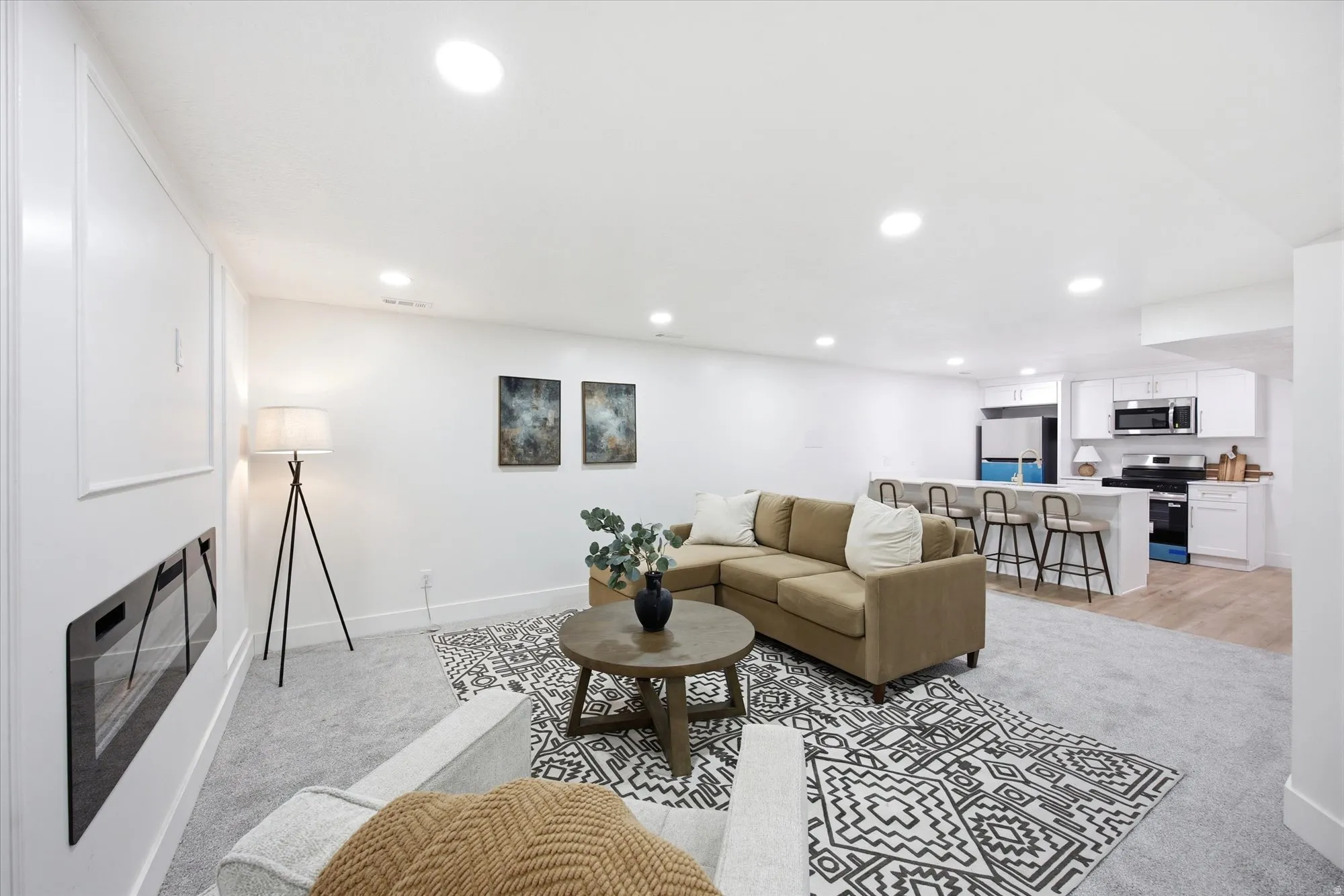 Open-concept living area featuring an integrated kitchen, contemporary electric fireplace, recessed lighting, and soft gray carpet