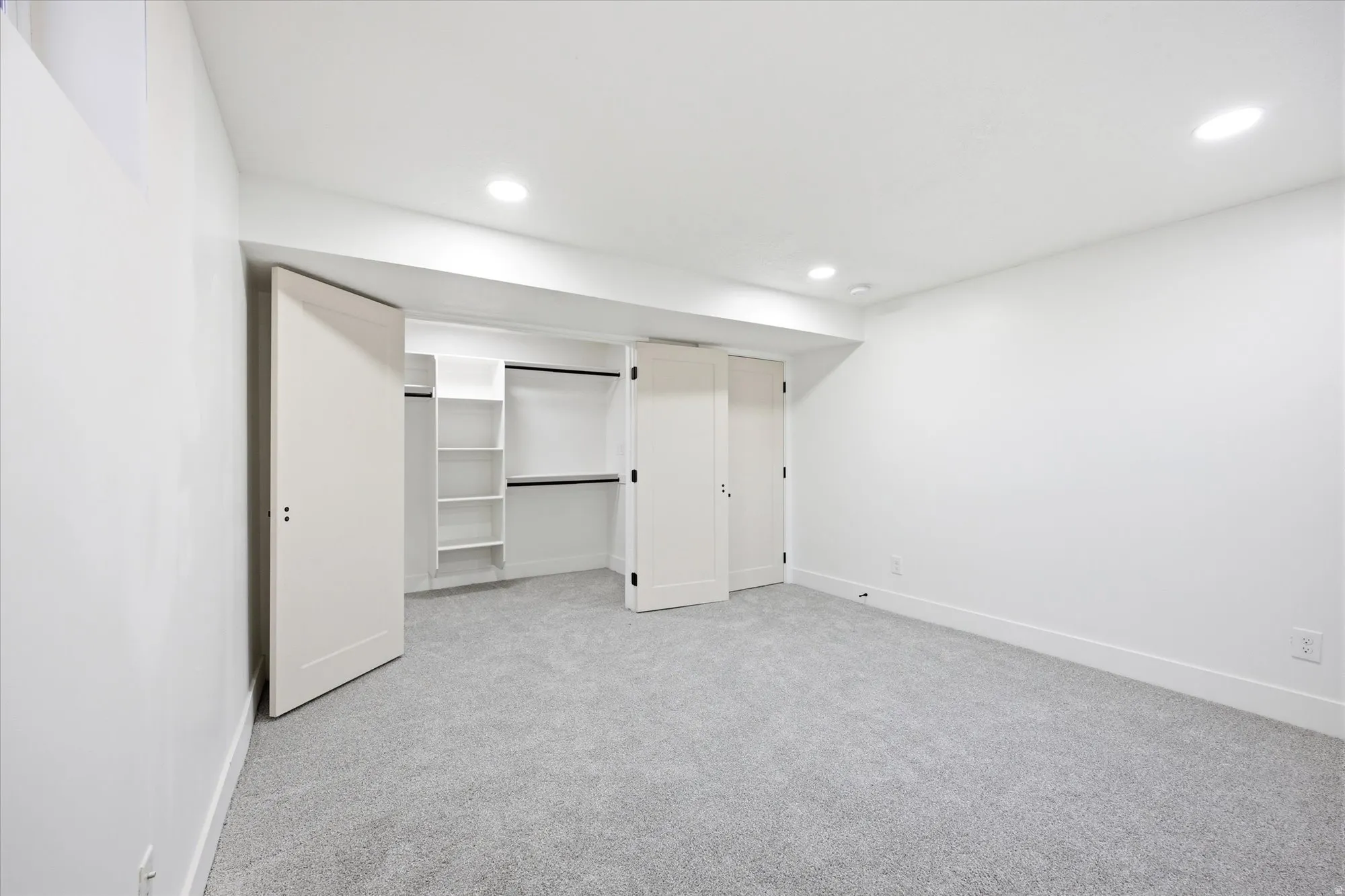 Bedroom featuring light gray carpeting, white walls, recessed ceiling lighting, and a closet with bifold doors and built-in shelving
