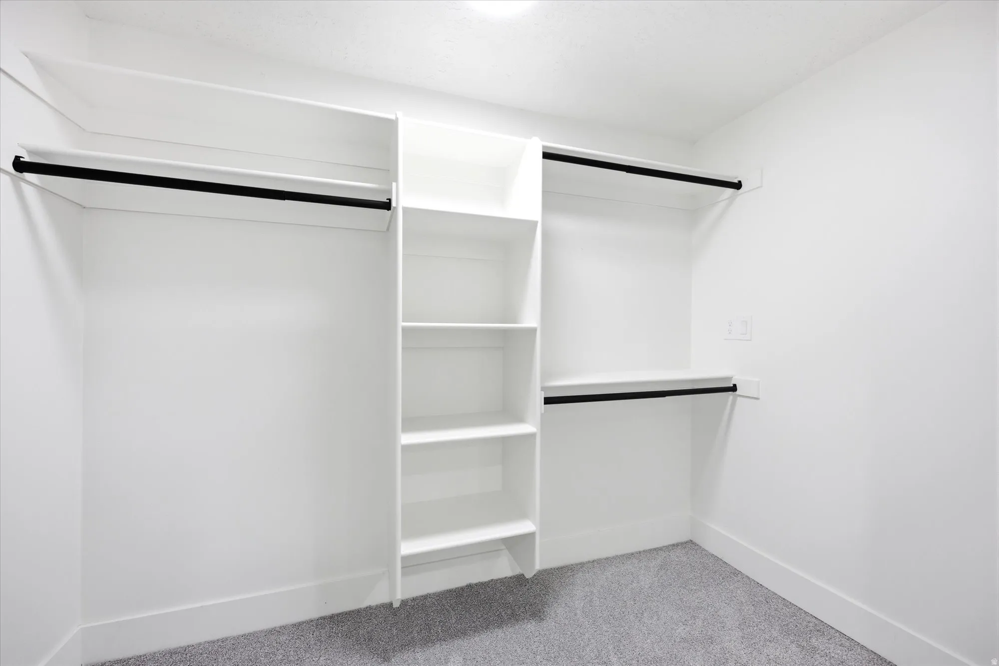 Spacious closet with white shelving, multiple hanging rods, and light gray carpeting