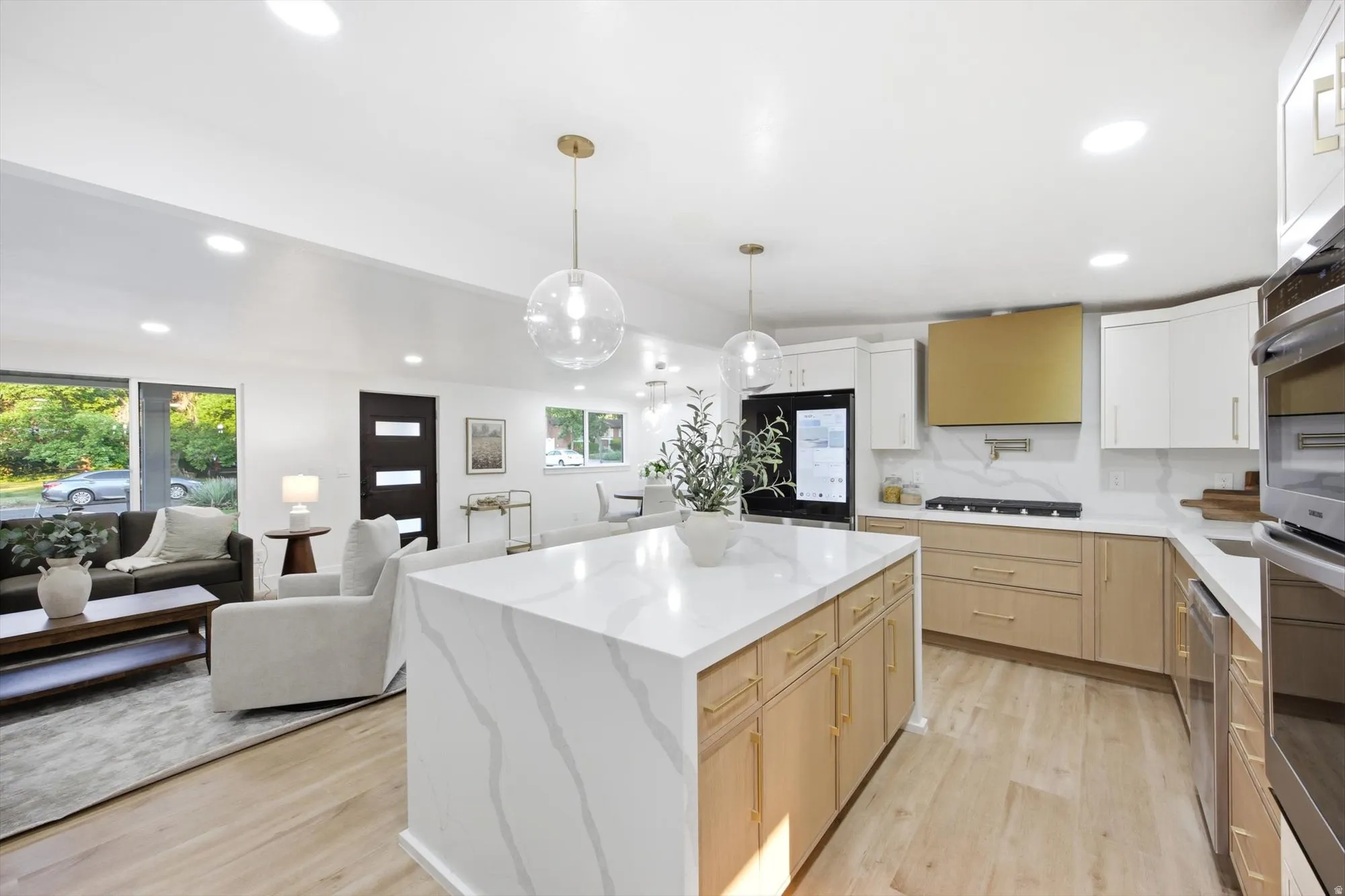 Open-concept kitchen and living area featuring a waterfall island with a quartz countertop, gold-toned hardware, recessed lighting, and wood-finish flooring