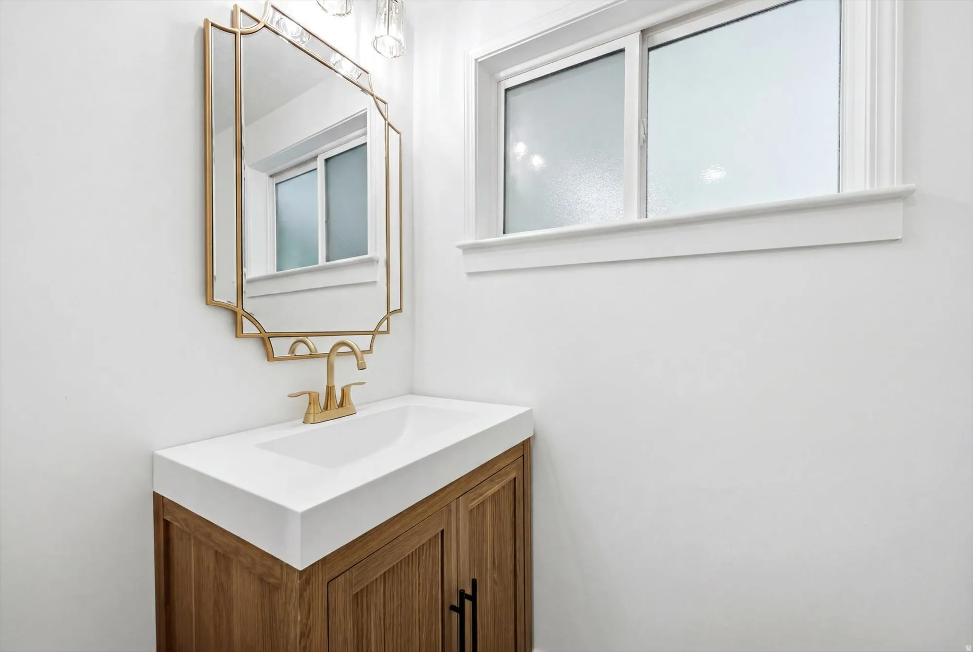 Bathroom vanity featuring a wood-finish cabinet with black hardware, a white integrated sink, and a gold-toned faucet