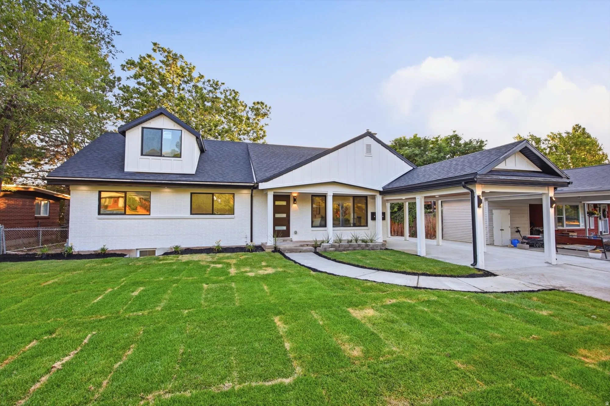 Contemporary residence featuring a white brick and vertical siding exterior, a dark shingle roof, a covered entry, a covered carport, and a dormer window