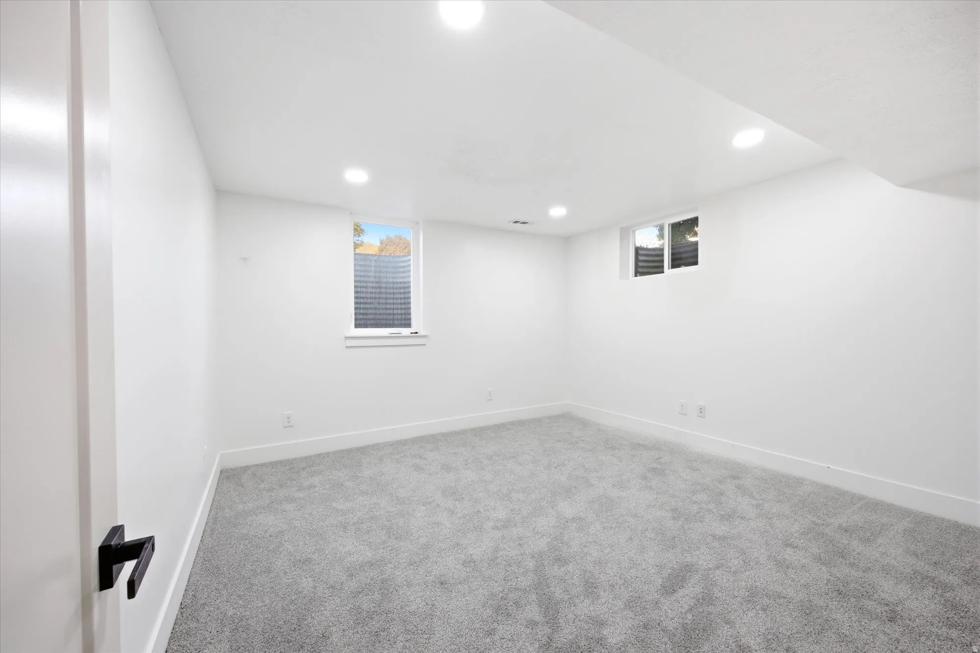 Bright room featuring light gray carpet, white walls, recessed lighting, and two windows