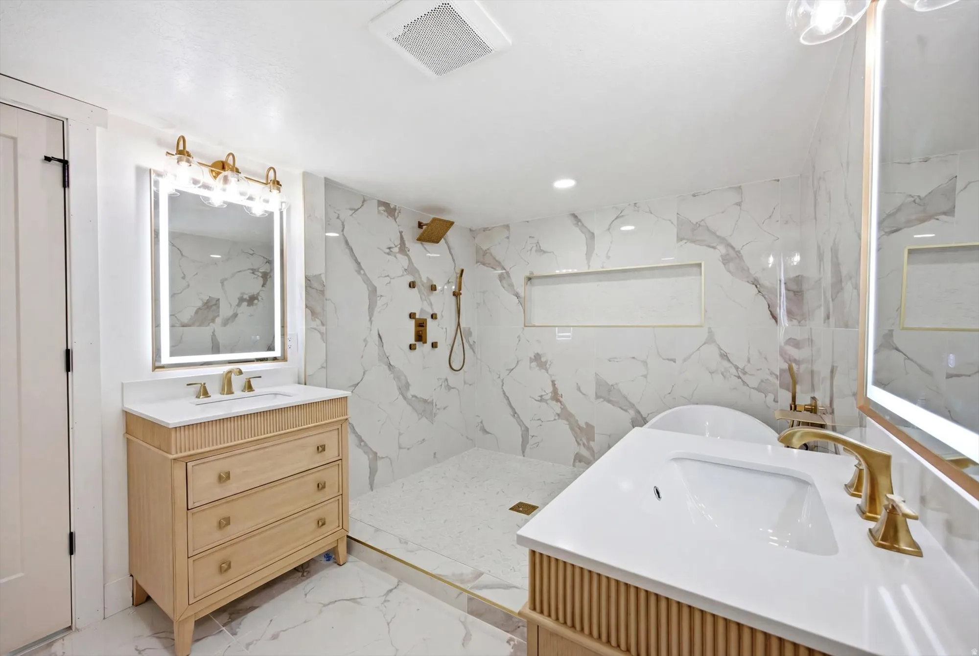 Bathroom featuring dual vanities with integrated sinks, quartz countertops, and brushed gold fixtures