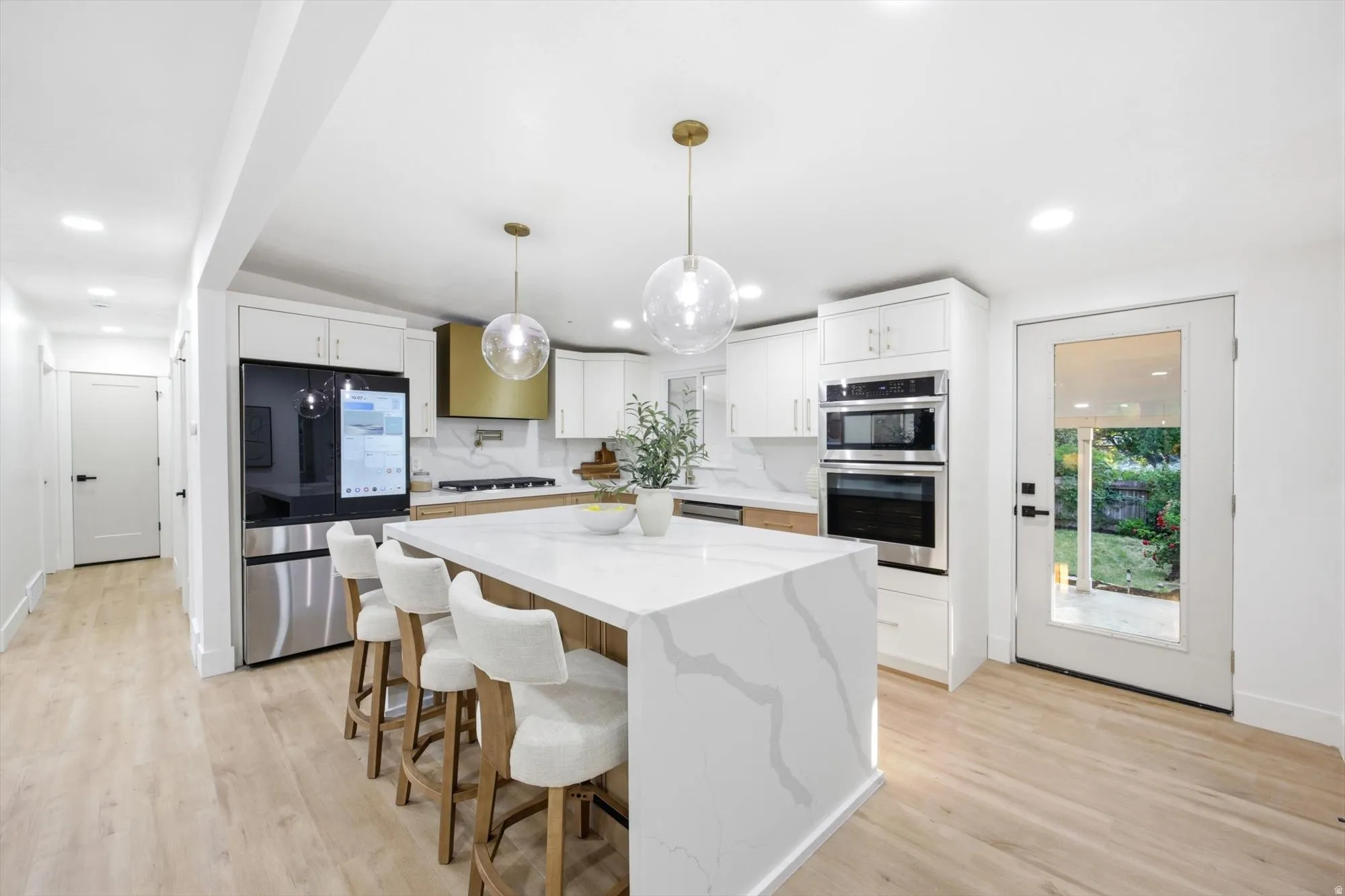 Modern kitchen featuring a waterfall island with stone countertop, white shaker cabinetry, stainless steel appliances, and wood-finish flooring
