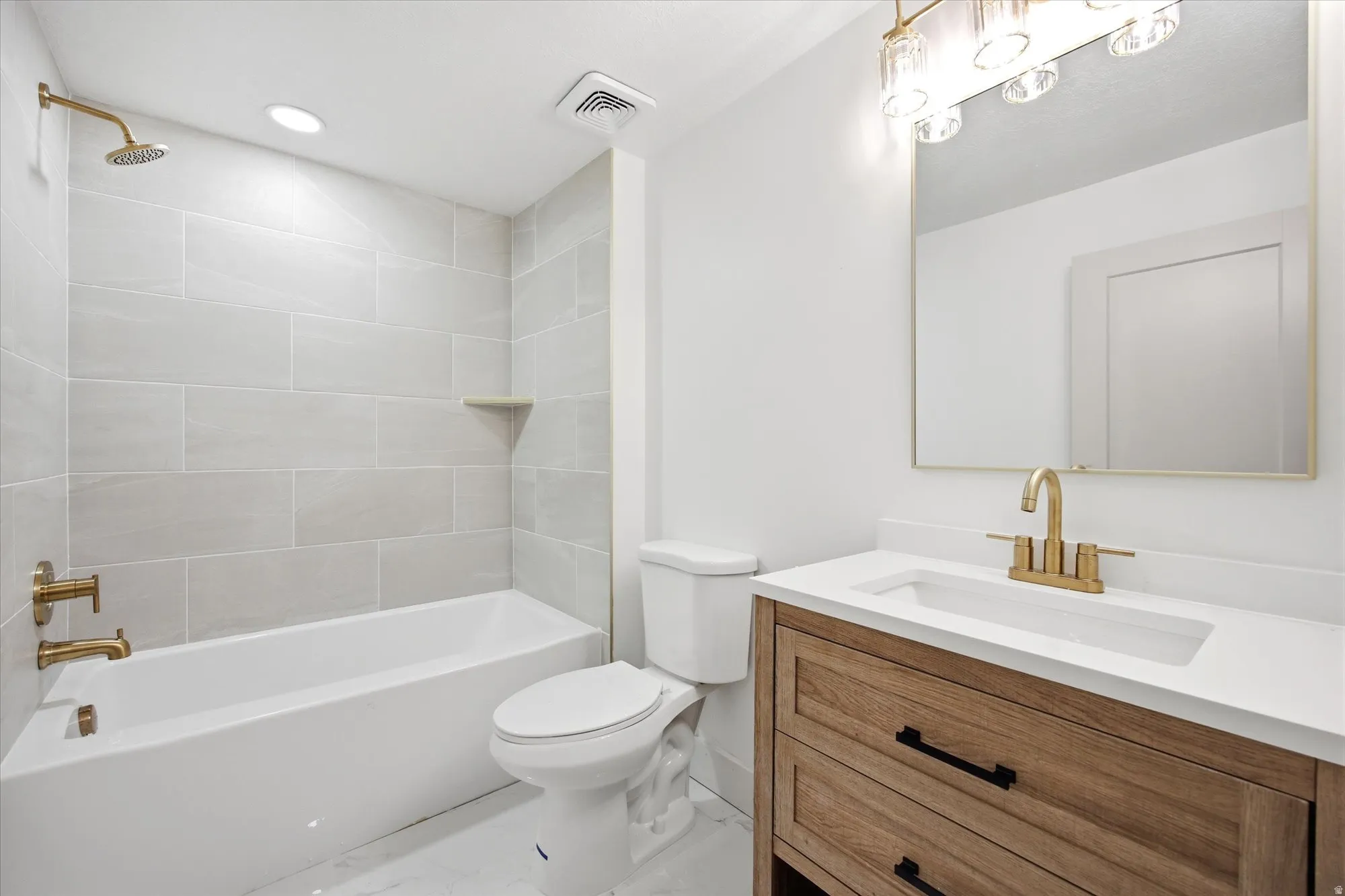 Contemporary bathroom featuring a white soaking tub with brass fixtures, a matching brass rain shower head, and light-toned rectangular wall tiling