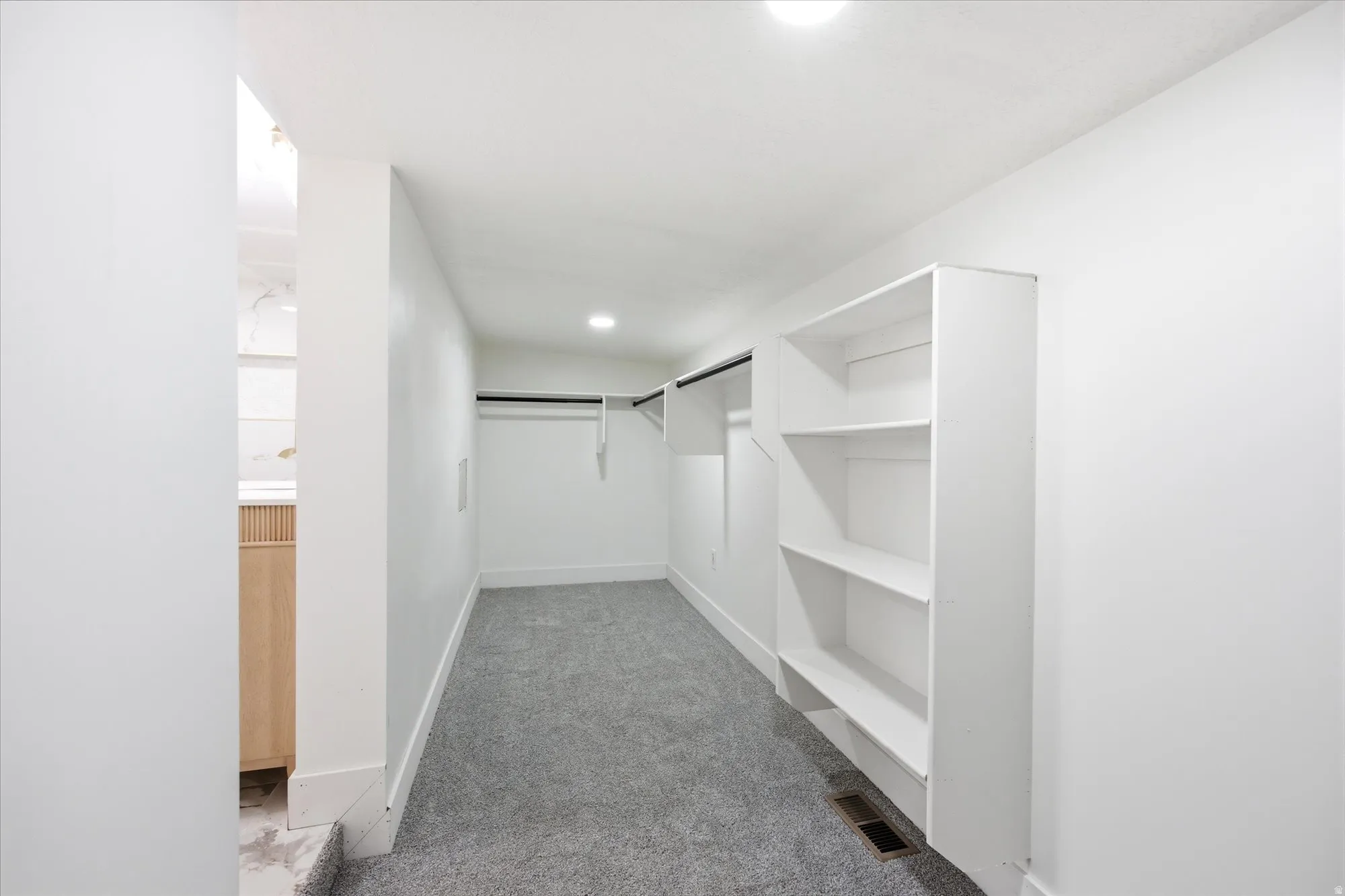Spacious walk-in closet featuring built-in shelving, hanging rods, recessed lighting, and gray carpeting