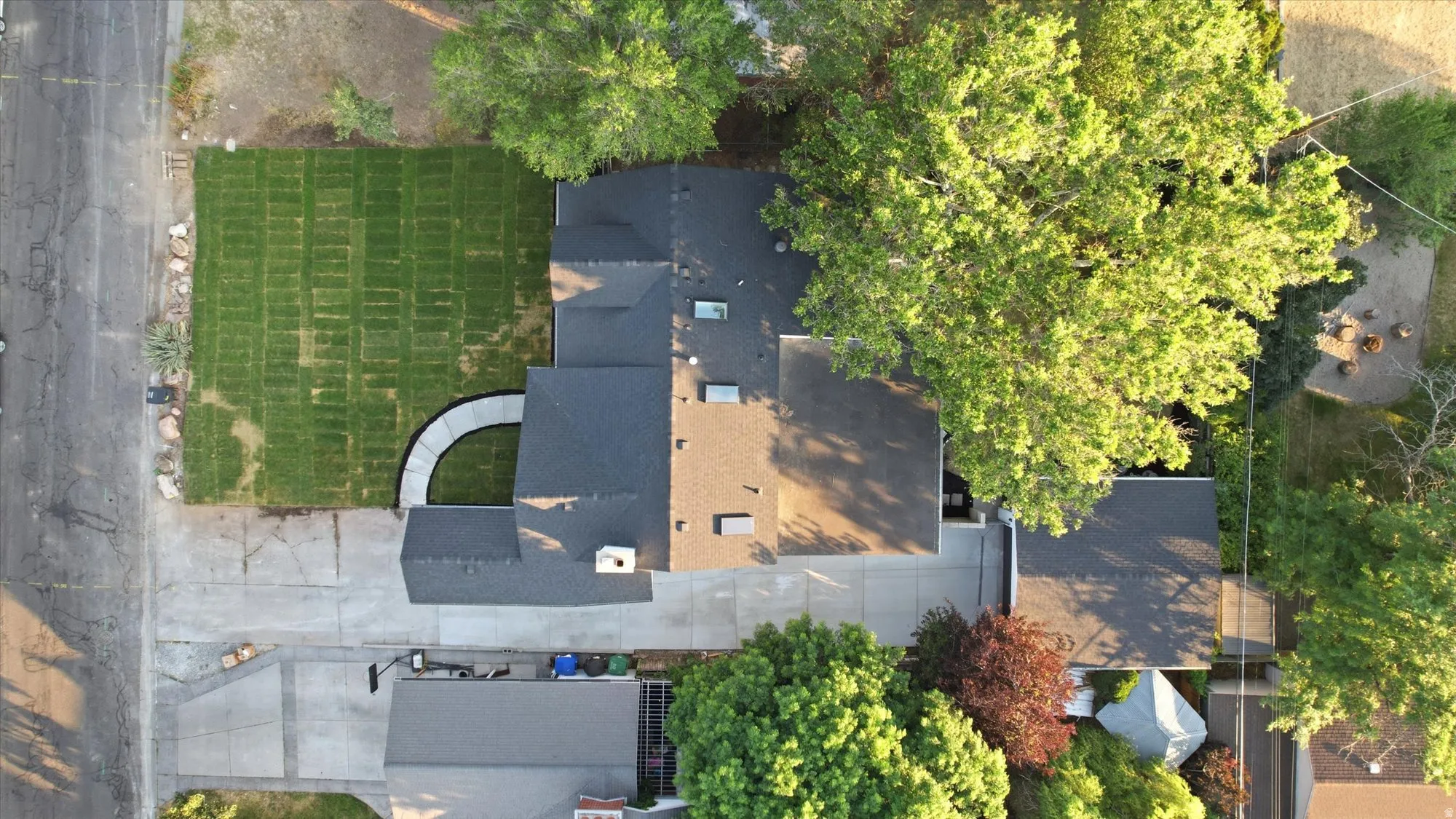 Aerial perspective showcasing a property with a newly installed sod lawn, a curved concrete pathway, mature trees, and a dark shingle roof
