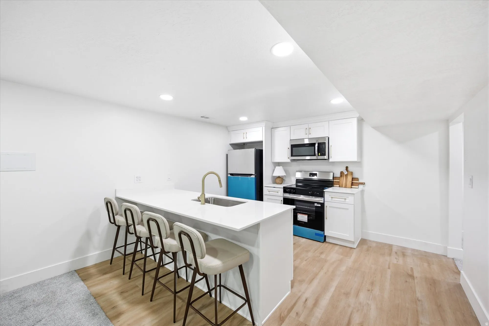 Modern kitchen featuring a large island with integrated sink and seating, white cabinetry, stainless steel appliances, and wood-finish flooring