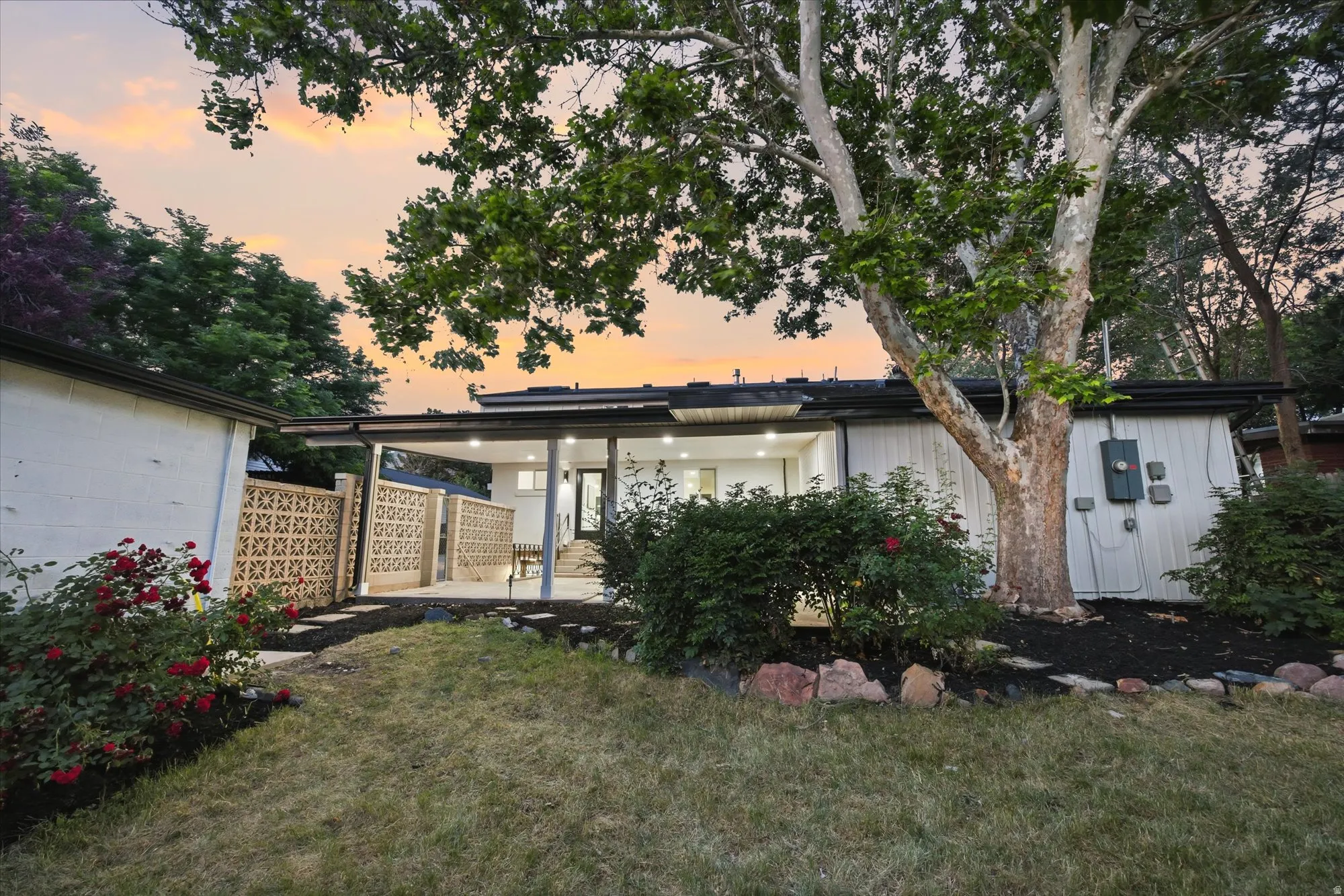 Expansive backyard with a covered patio, a stone pathway, mature trees, and a decorative block wall