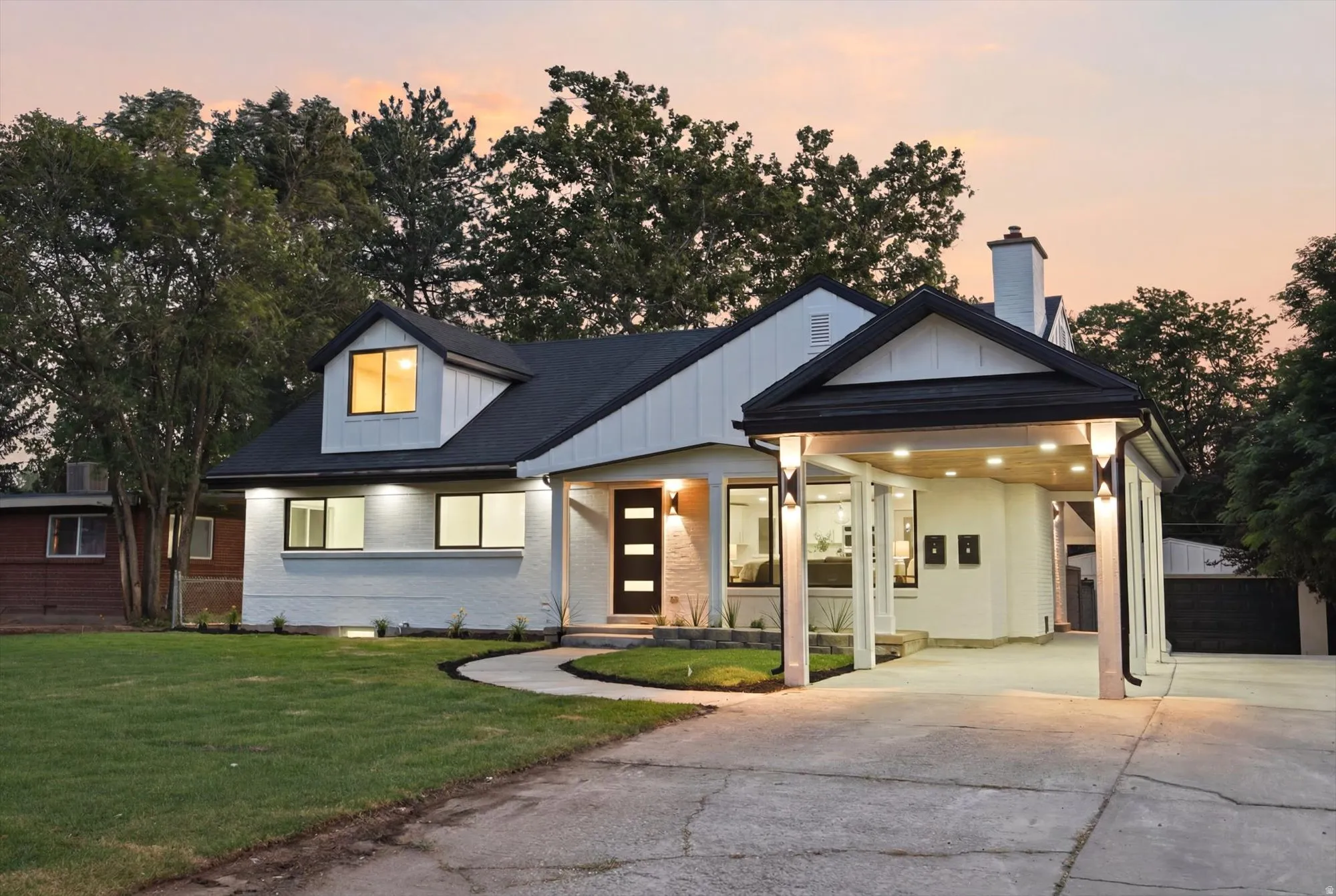 Modern farmhouse exterior featuring white painted brick, black trim, a gabled roofline, and a prominent covered carport with recessed lighting