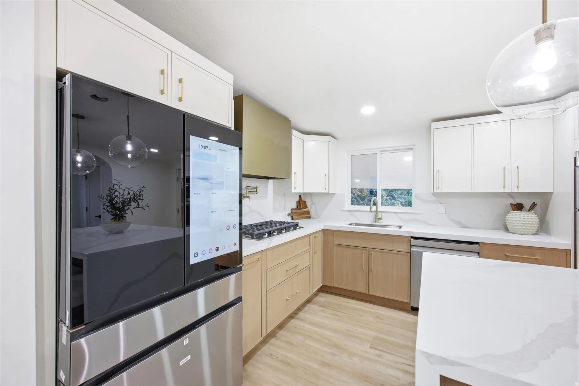 Contemporary kitchen featuring two-tone cabinetry, quartz countertops, a gas range with a gold-tone range hood, and a built-in smart refrigerator