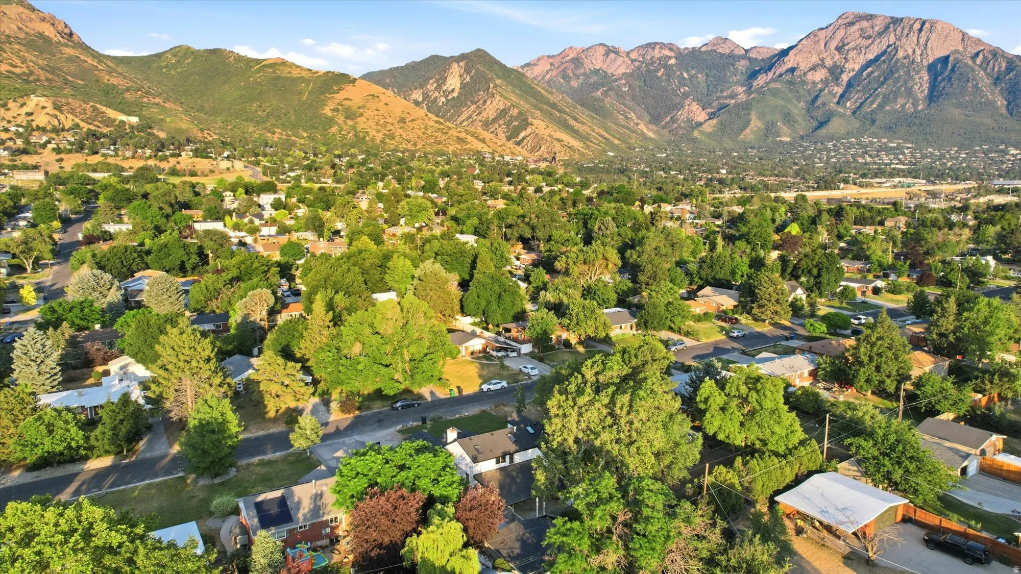 Lush suburban residential area nestled at the base of prominent mountains, featuring mature tree canopies