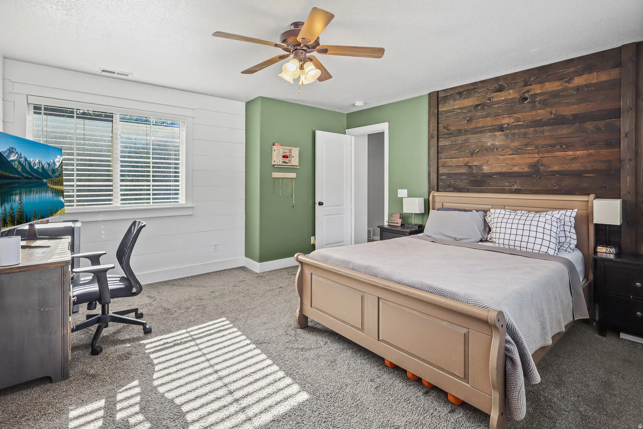Spacious room featuring a prominent wood plank accent wall, neutral carpeting, and a ceiling fan with integrated lighting