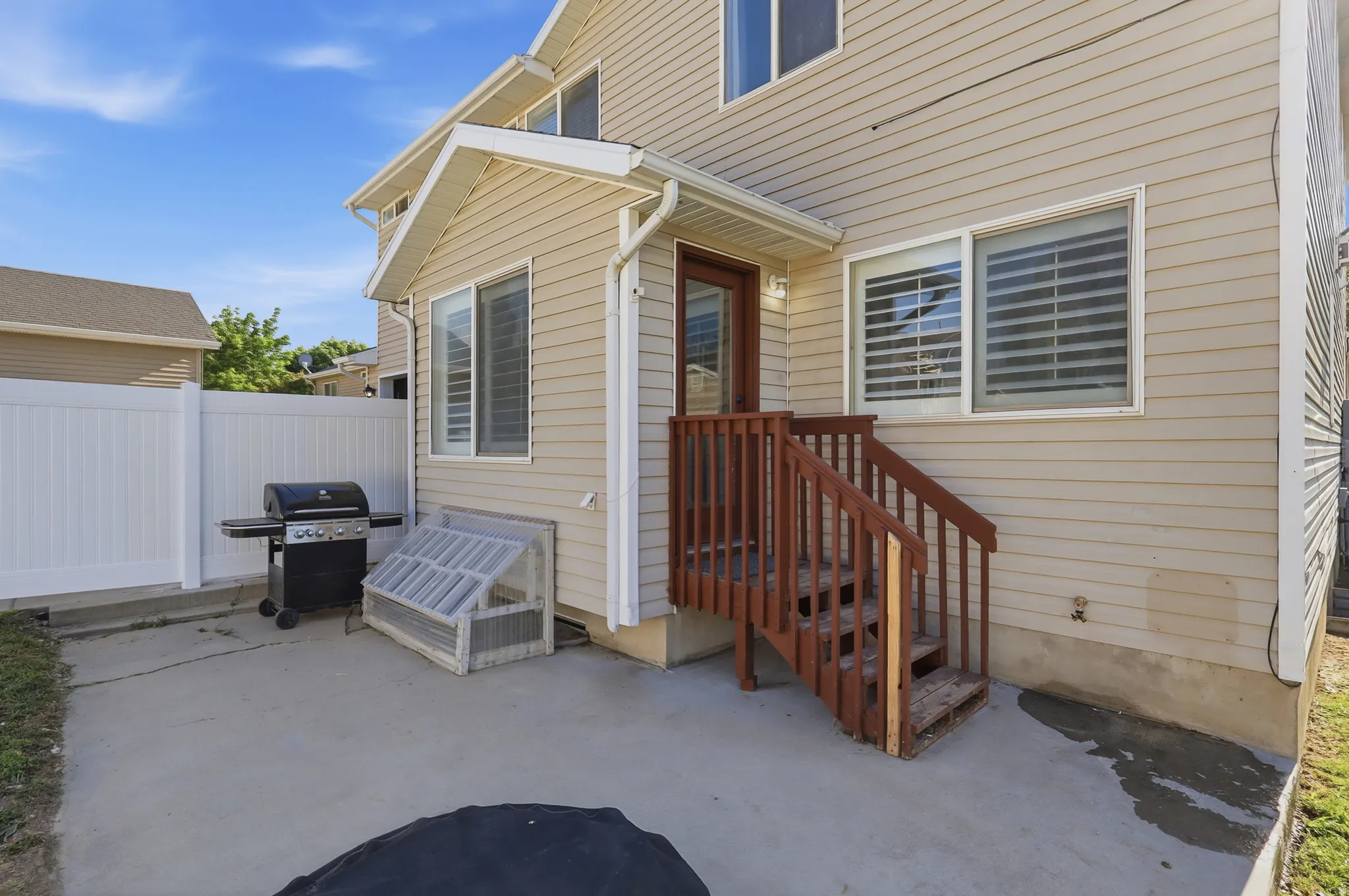 Exterior patio area featuring a concrete surface, tan siding, white vinyl fencing, and a wood-finish staircase leading to an upper-level door