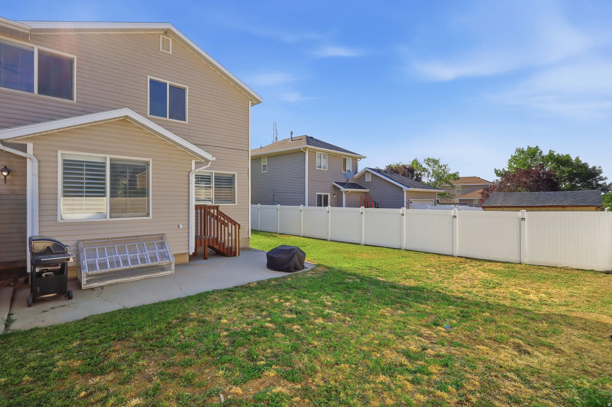Expansive backyard featuring a large green space, a full privacy fence, and a concrete patio with exterior access