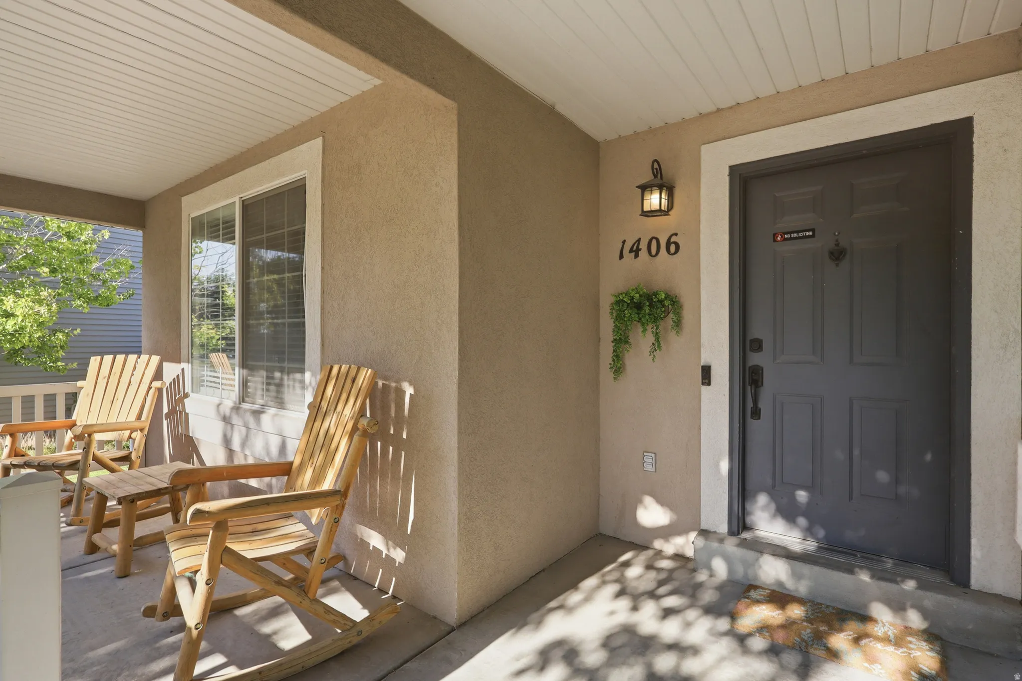 Covered front porch featuring a dark gray paneled entry door with a door knocker, an outdoor sconce, and house numbers