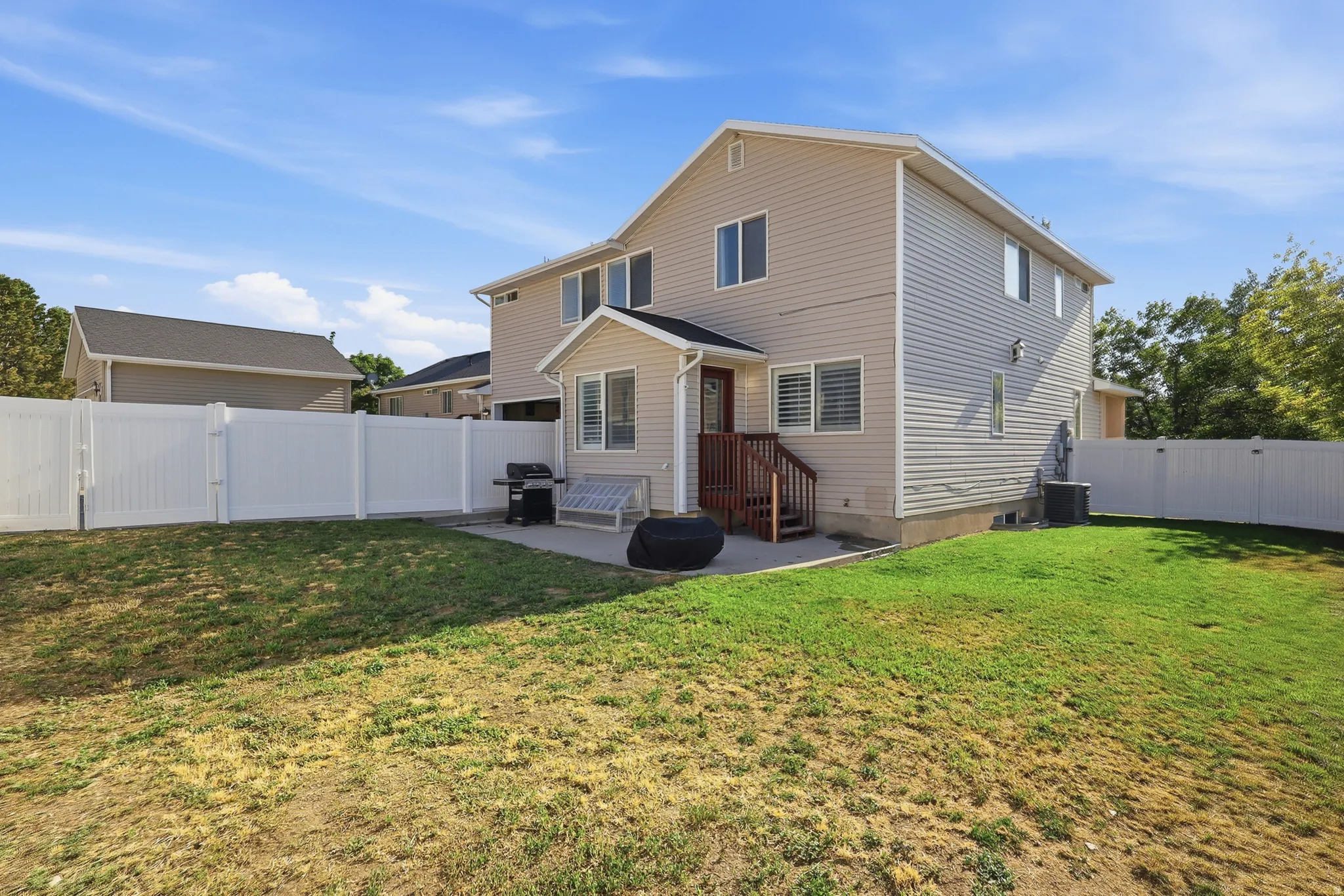 Expansive backyard featuring a manicured lawn, full privacy fencing, a concrete patio, and a deck with stairs providing exterior access