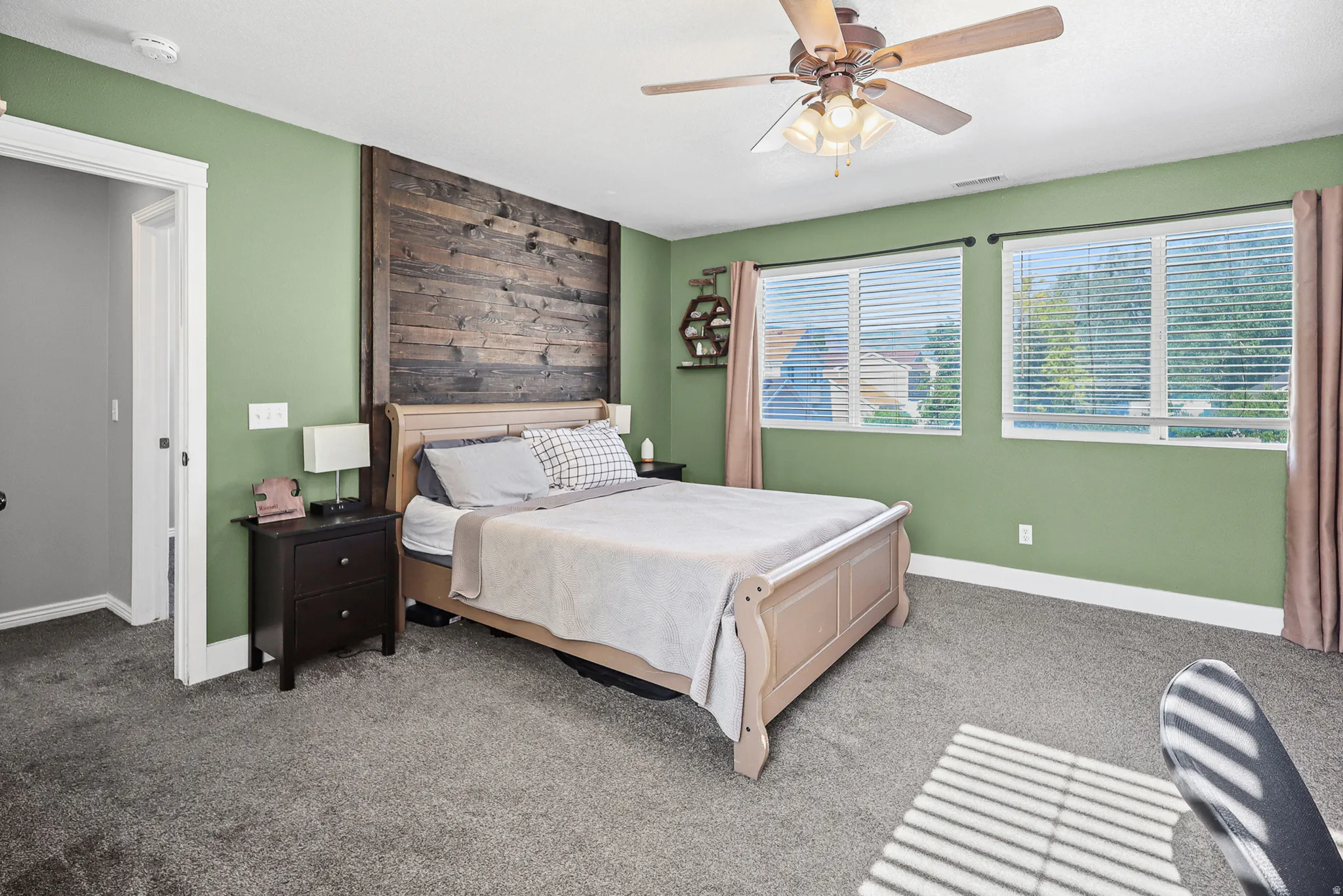 Spacious room featuring a decorative wood plank accent wall, dual windows with blinds, and a ceiling fan with integrated lighting
