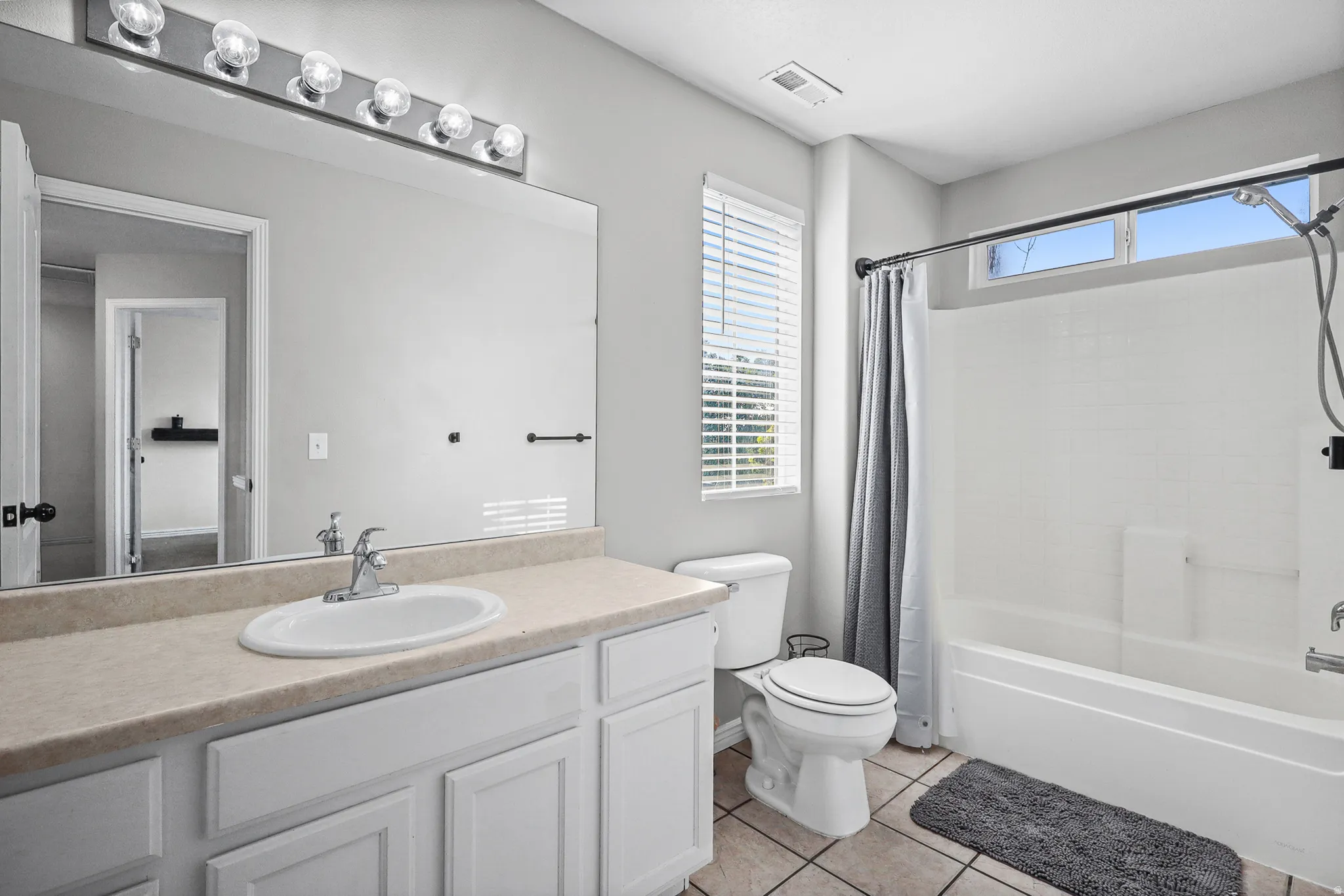 Bathroom featuring a single vanity with a laminate countertop, white cabinetry, and a full-width mirror