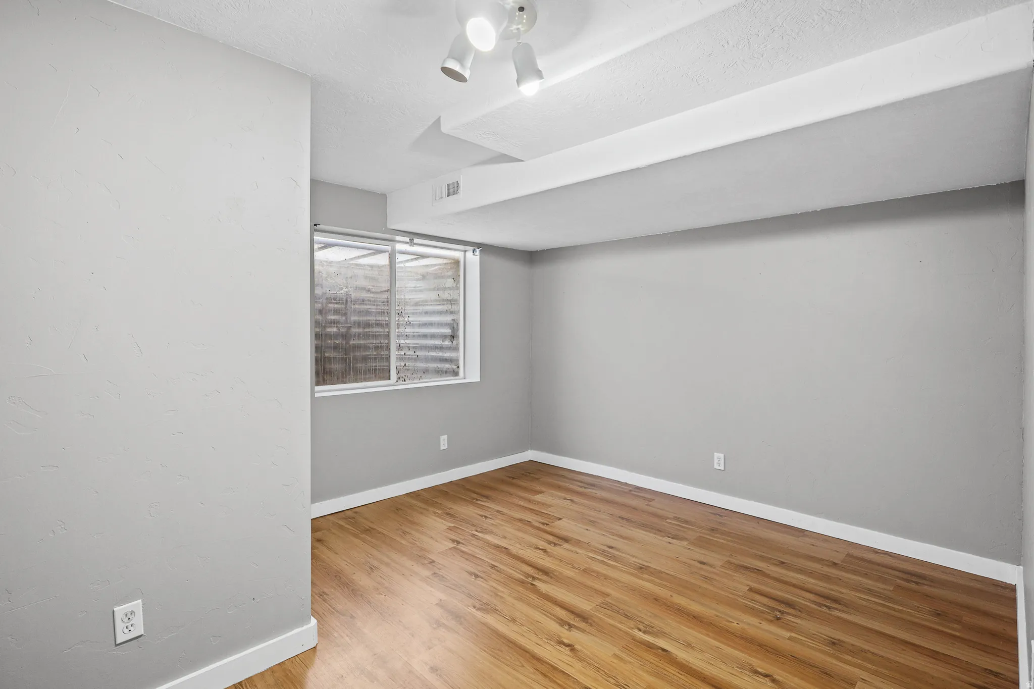 Room featuring wood-finish flooring, light gray walls, white trim, and a window with a window well