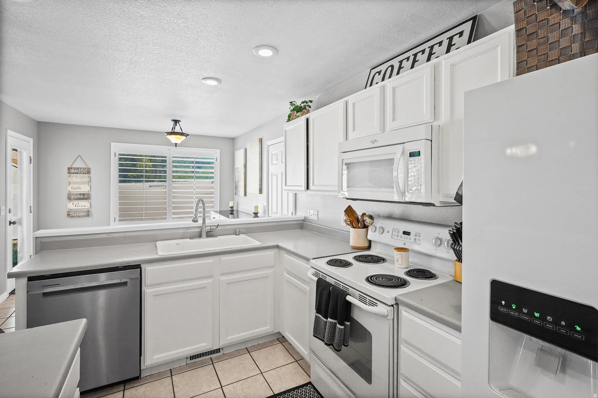 Well-appointed kitchen featuring white cabinetry, light countertops, stainless steel dishwasher, white range, and white built-in microwave