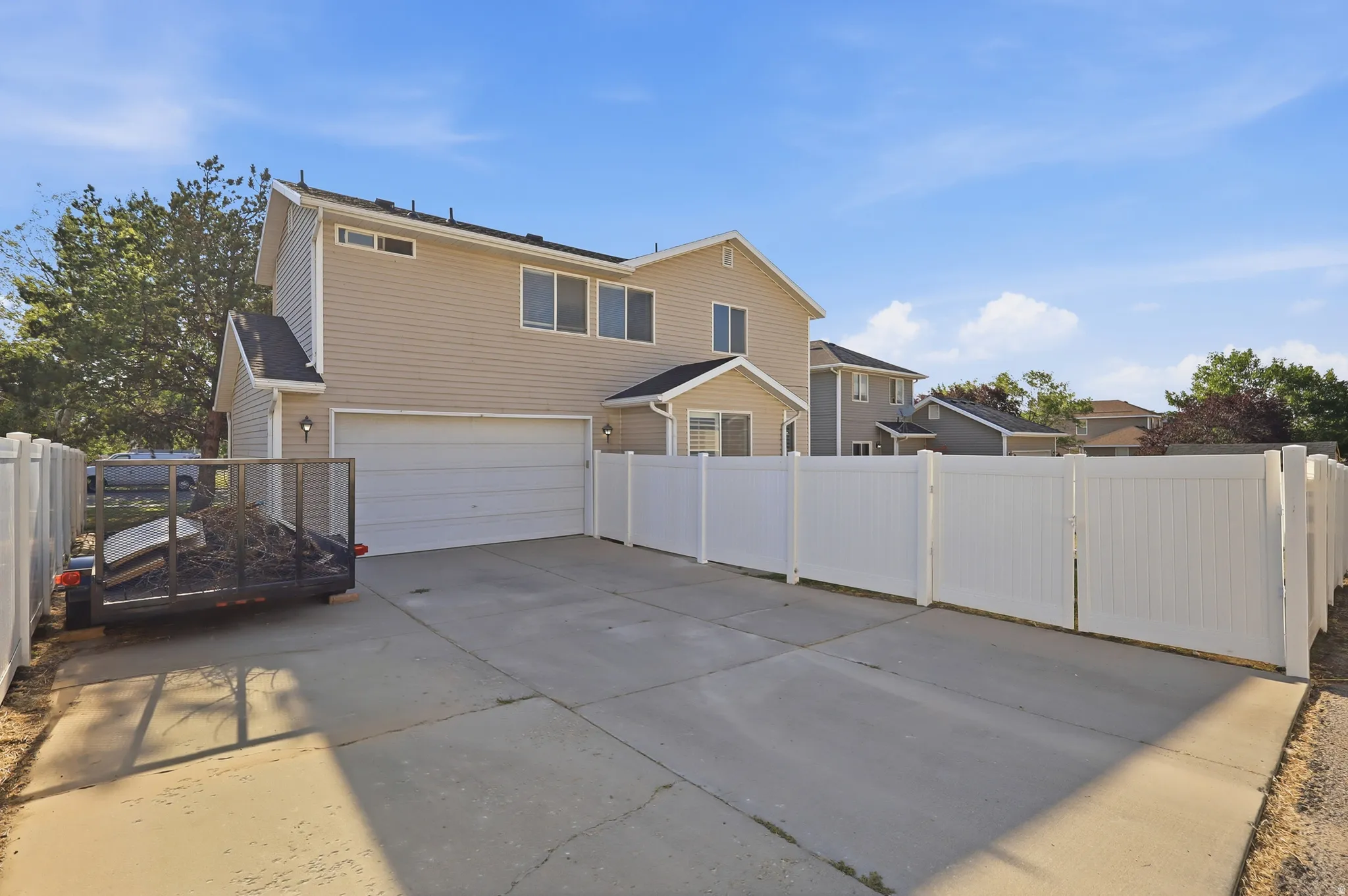 Rear exterior featuring two-story construction, attached garage, concrete driveway, vinyl siding, and white privacy fencing