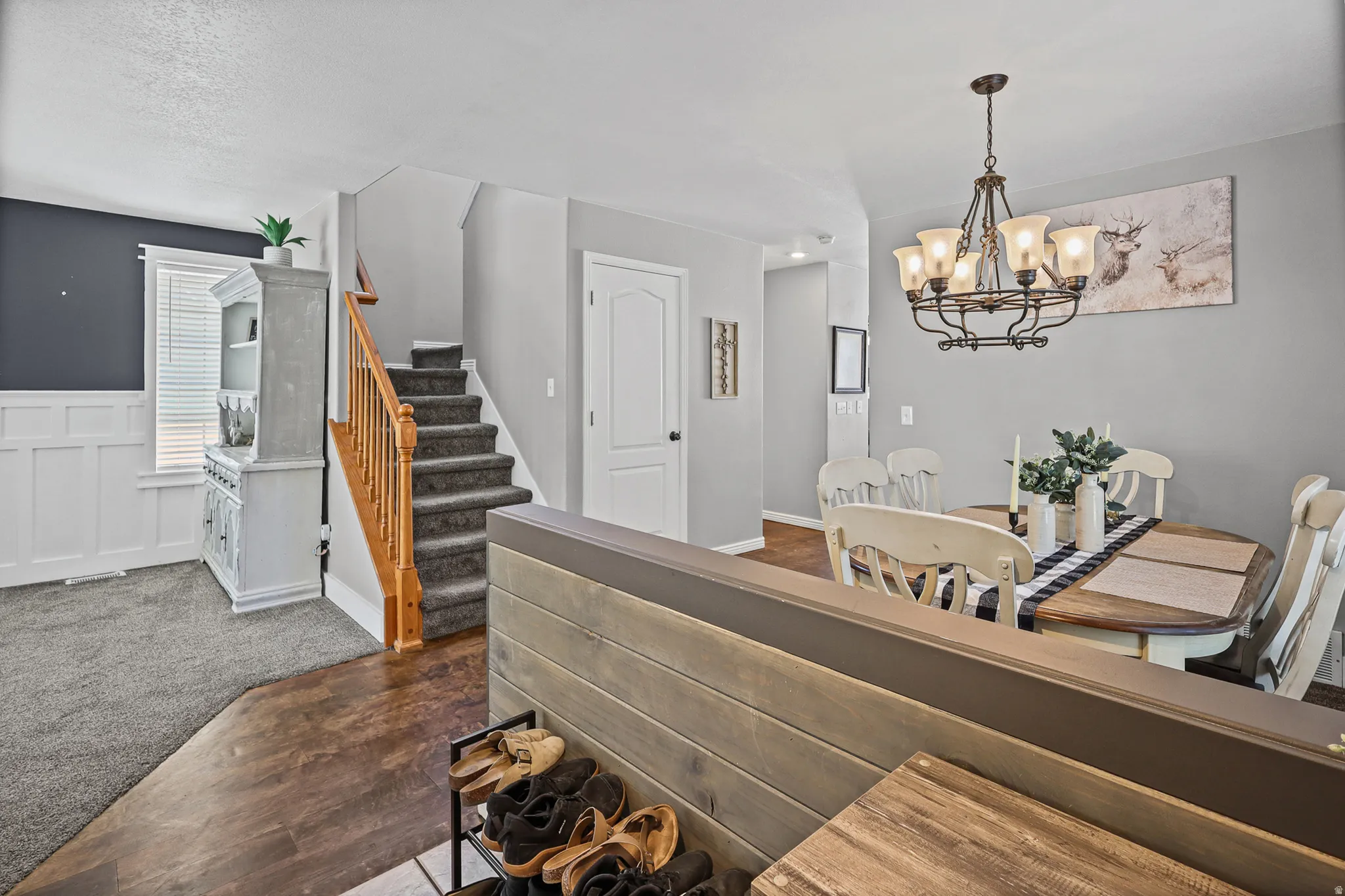Open living area featuring wood-finish flooring, a carpeted staircase with a wood handrail, and white wainscoting