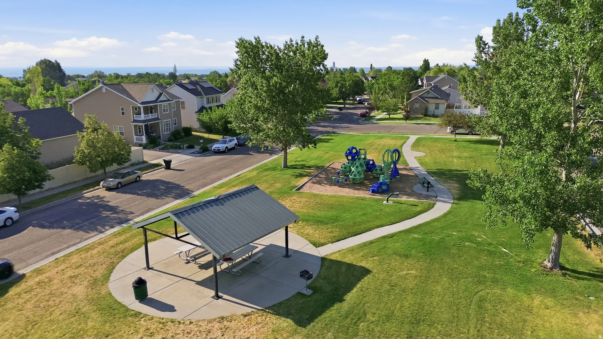 Neighborhood park featuring a covered picnic area with concrete pad, playground equipment, and paved walking paths