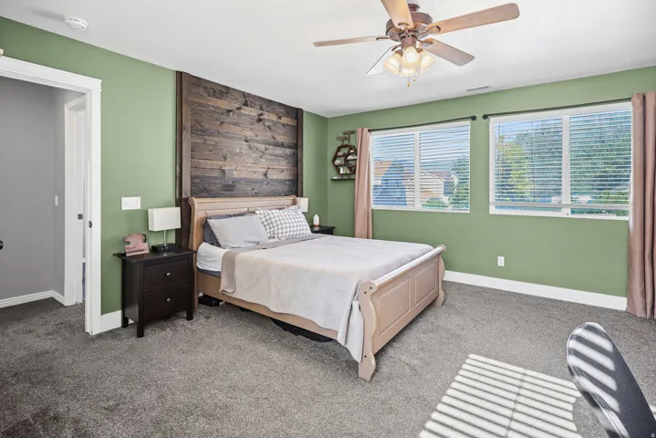 Spacious room featuring a decorative wood plank accent wall, dual windows with blinds, and a ceiling fan with integrated lighting