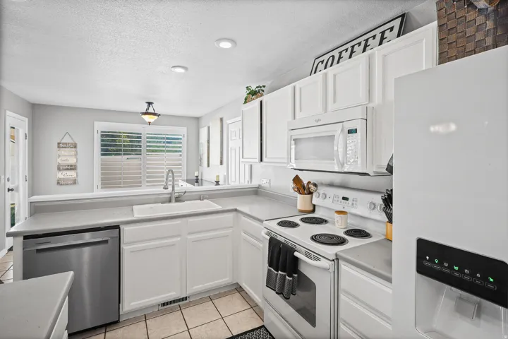 Well-appointed kitchen featuring white cabinetry, light countertops, stainless steel dishwasher, white range, and white built-in microwave
