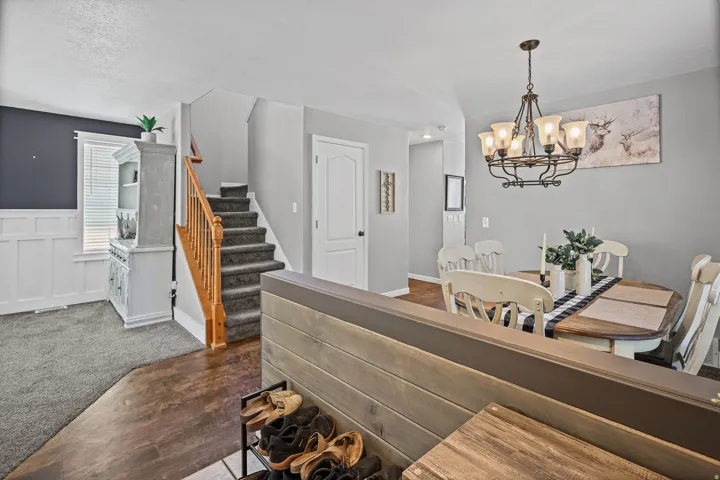Open living area featuring wood-finish flooring, a carpeted staircase with a wood handrail, and white wainscoting