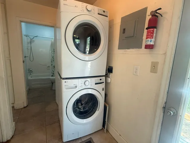 Laundry area with stacked washer and dryer, tile flooring, and a nearby full bathroom featuring a tub with shower