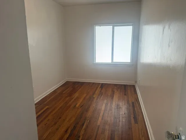 Room featuring wood-finish flooring, white baseboards, and a white window frame