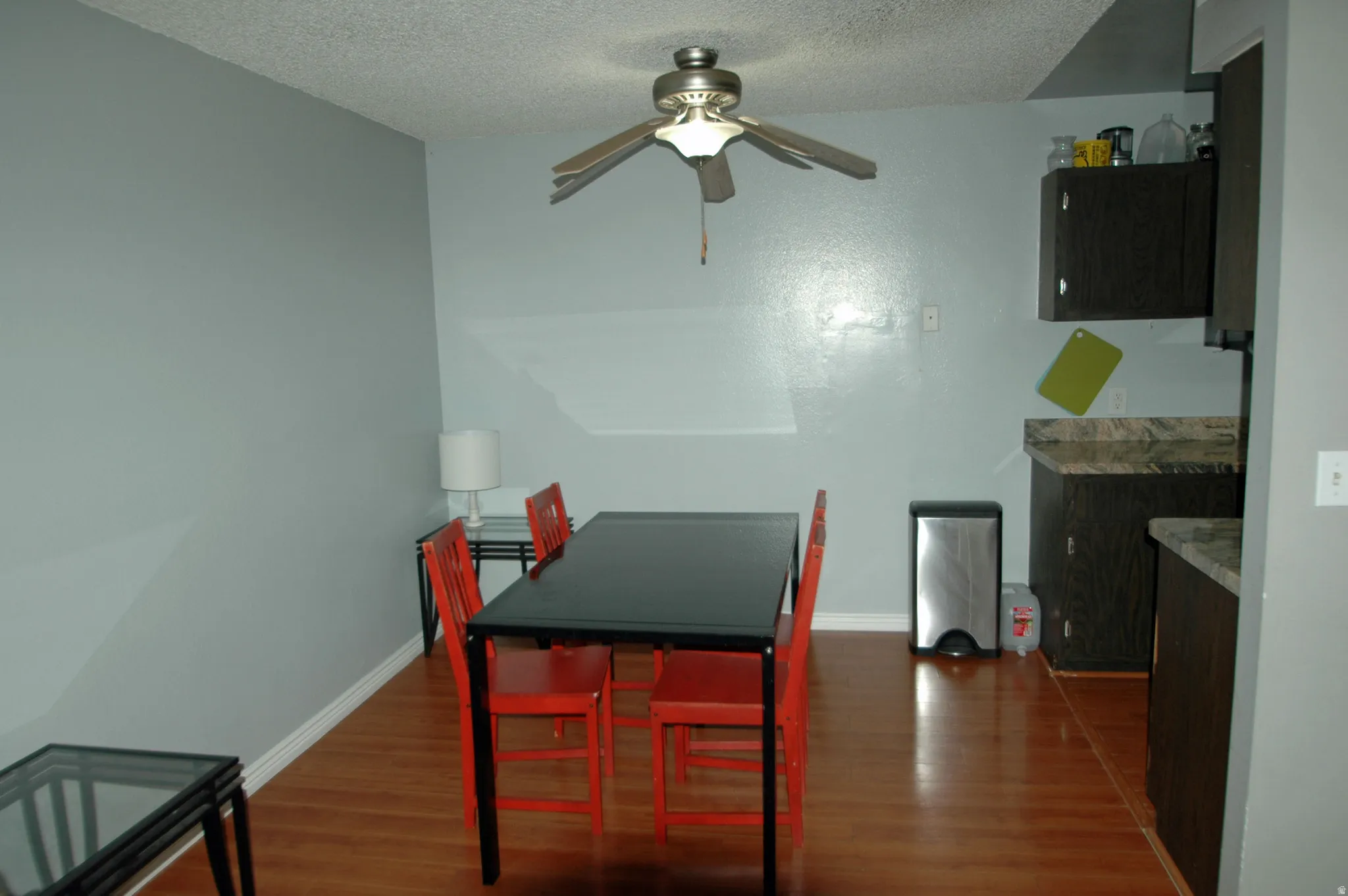 Combined dining and kitchen area featuring wood-finish flooring, a ceiling fan fixture, and dark wood-finish cabinetry with stone-look countertops