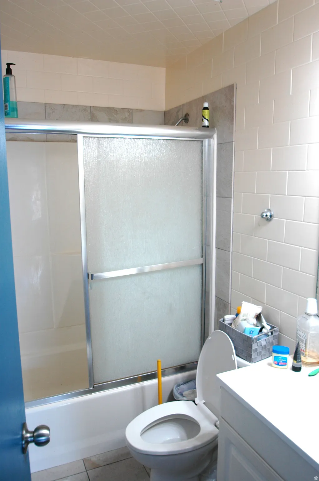 Bathroom featuring a white subway tile surround, gray accent tiling, a tub with sliding glass doors, a white toilet, and a white vanity with a cabinet base