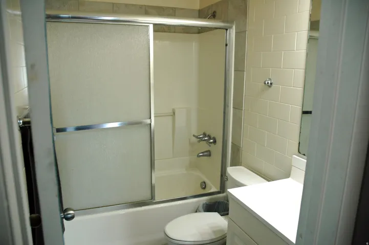 Full bathroom featuring a white vanity with a white countertop, subway-tiled walls, and a shower-over-tub combination with sliding glass doors