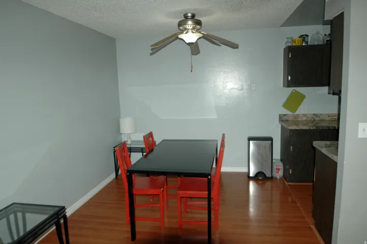 Combined dining and kitchen area featuring wood-finish flooring, a ceiling fan fixture, and dark wood-finish cabinetry with stone-look countertops