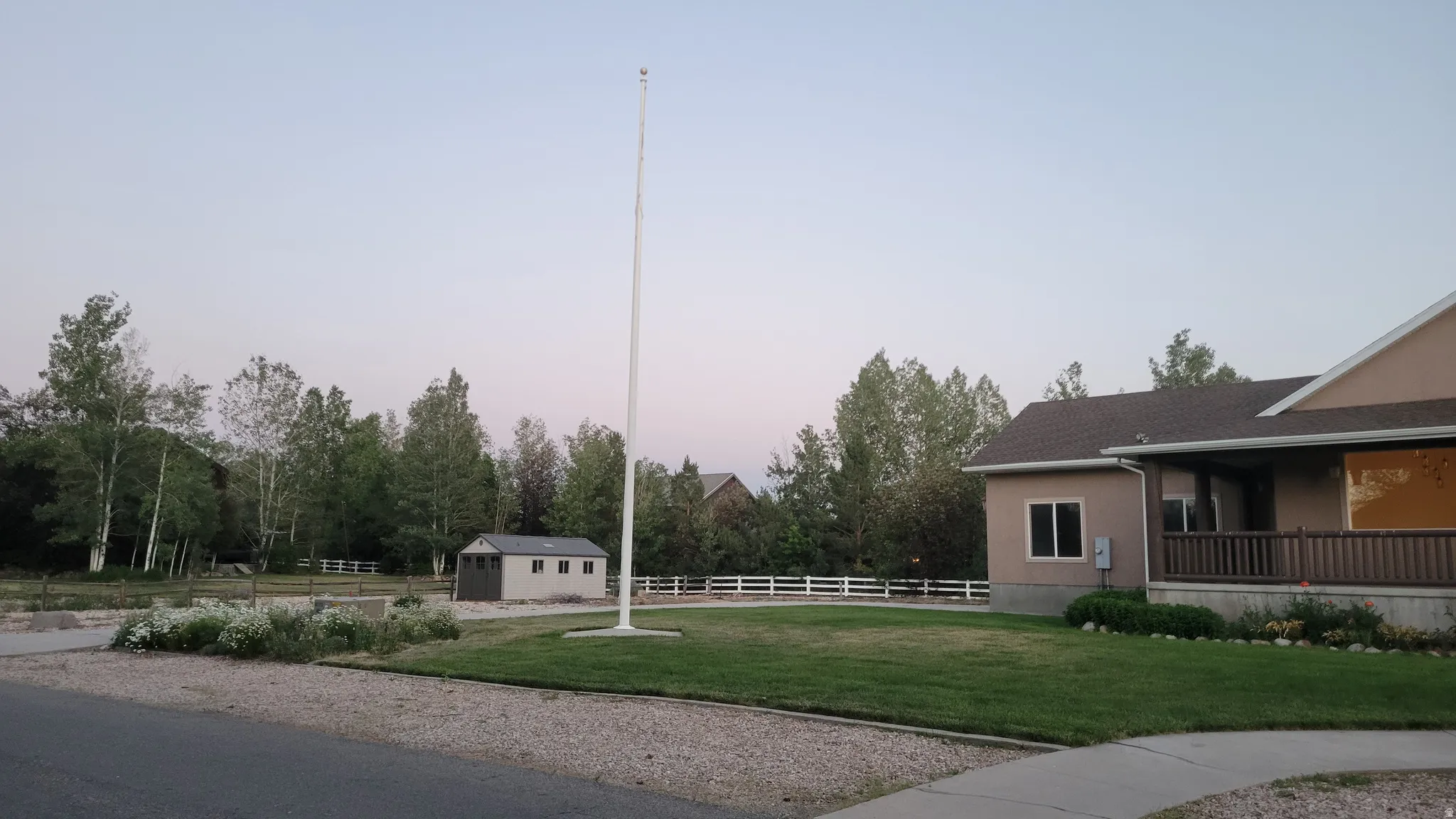 Expansive front yard featuring a manicured lawn, gravel driveway, and mature landscaping
