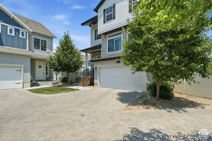 Paver driveway, attached garage, exterior siding, mature trees, and covered entry
