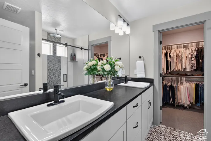 Dual undermount sinks with matte black fixtures, dark countertop, white vanity cabinetry, patterned tile flooring, and an organized closet system