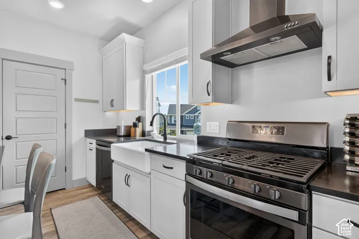 White cabinetry with dark hardware, stainless steel appliances, dark countertops, a farmhouse sink with a gooseneck faucet, and wood-finish flooring