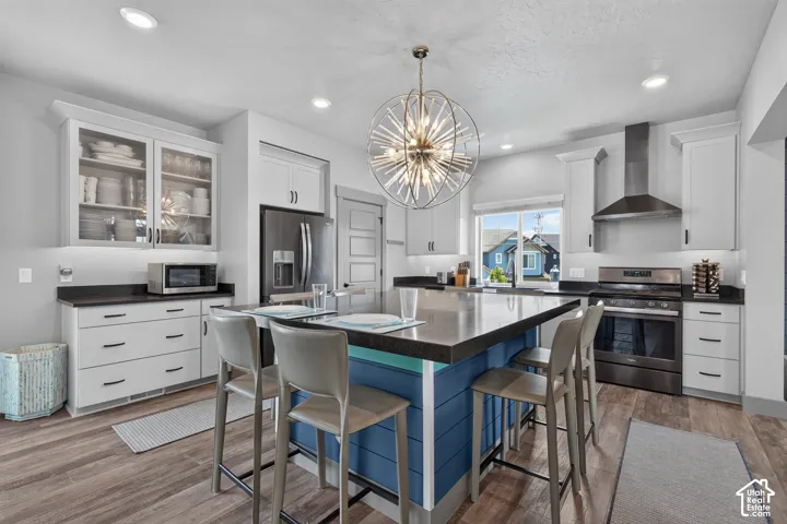 Kitchen featuring an oversized island, stainless steel appliances, white cabinetry, dark countertops, and wood-finish flooring