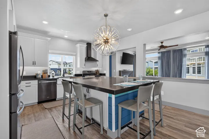 Contemporary kitchen featuring an oversized island with seating, stainless steel appliances, white cabinetry, LVP flooring, and a decorative pendant light fixture